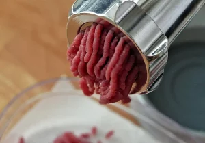 Metalowa maszynka do mielenia mięsa z czerwonym przemielonym mięsem nad miską